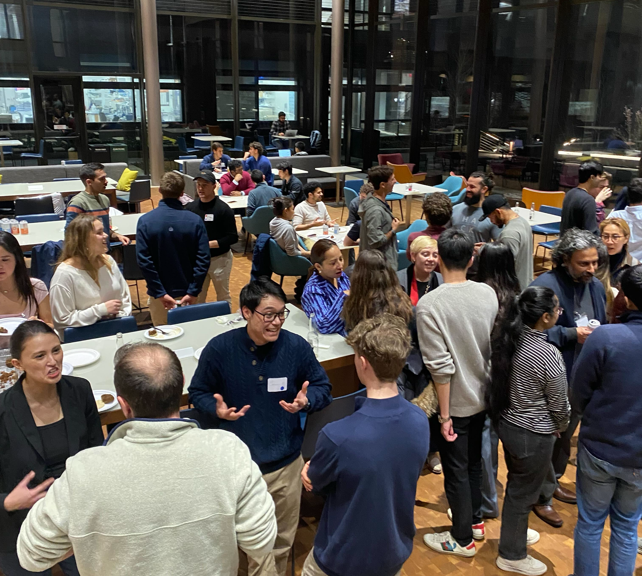 Event photo: attendees talking in groups across the café at the launch mixer